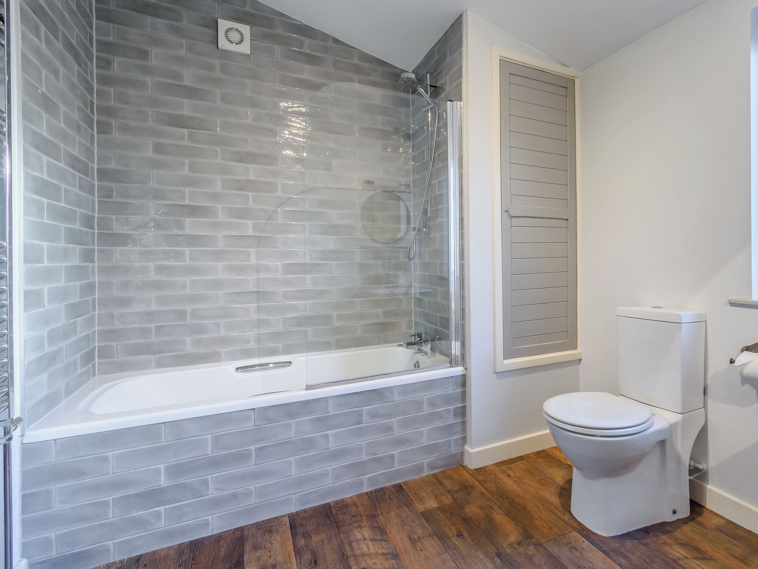 A bathroom with a glass-enclosed shower, a white toilet, and a wooden floor.