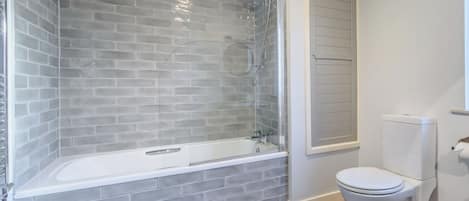 A bathroom with a glass-enclosed shower, a white toilet, and a wooden floor.