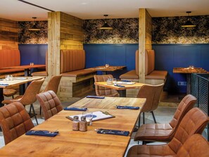 A restaurant with wooden tables and booths, leather seating, and blue walls with floral wallpaper.