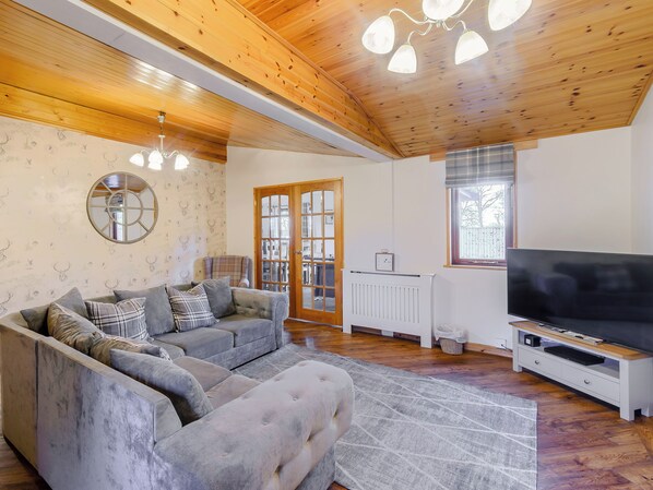 A living room with a grey sofa, a TV, and a wooden ceiling.