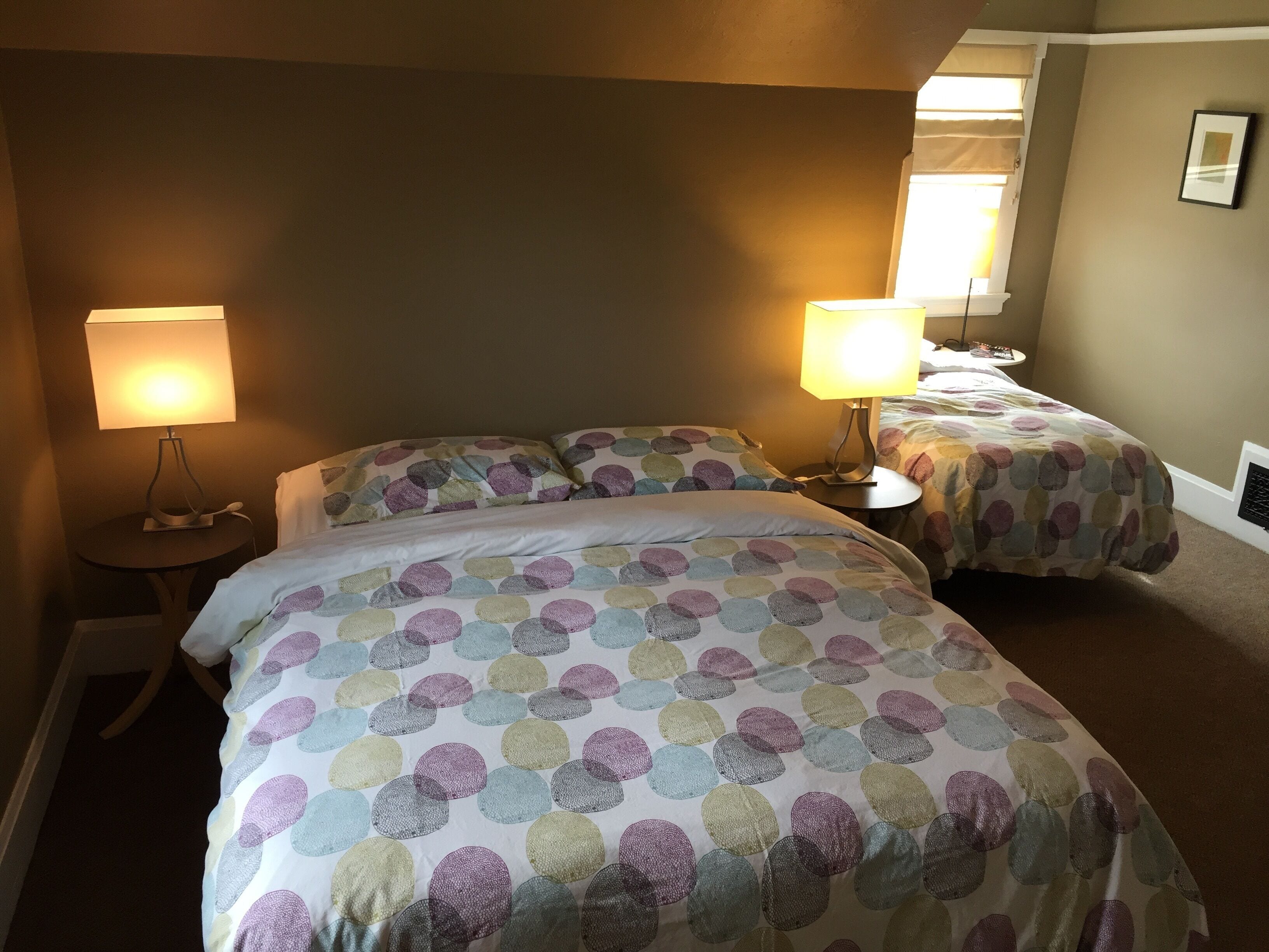 Habitación de hotel con dos camas, cada una con una colcha de estampado circular, dos lámparas de noche y un cuadro enmarcado en la pared.