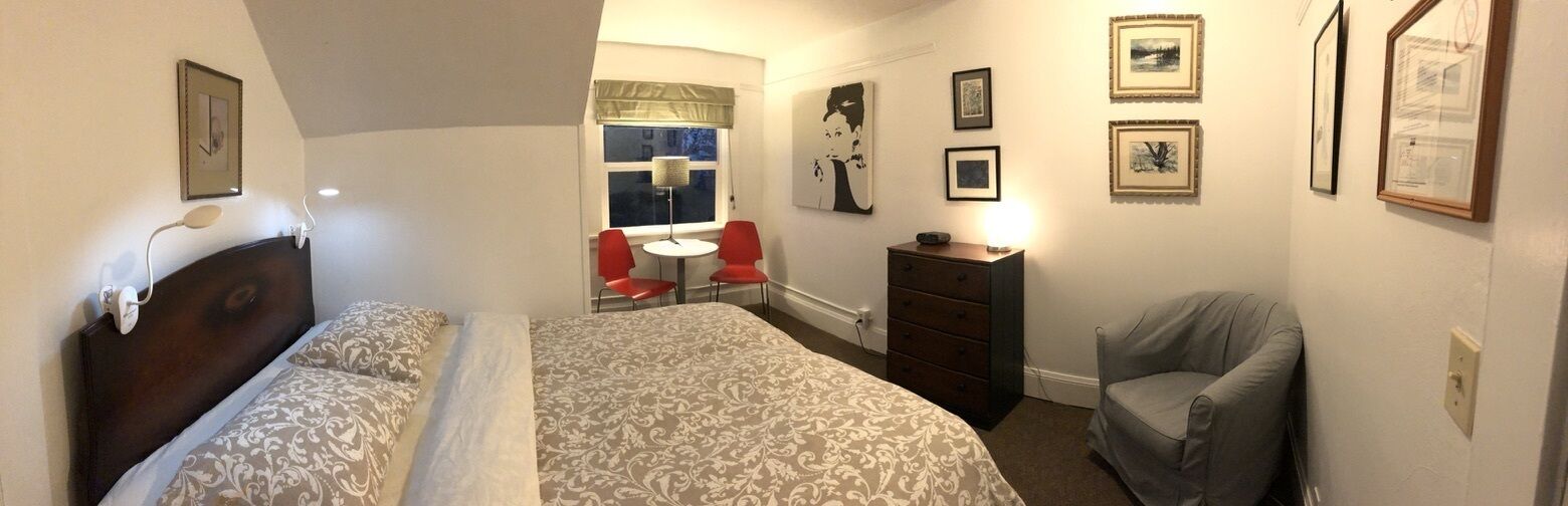 A bedroom with two beds, a desk with two chairs, a dresser, and artwork on the walls.