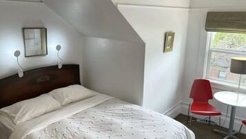 Ein Schlafzimmer mit einem Bett, einem roten Sessel, einem kleinen Tisch und einem Fenster mit Blick.