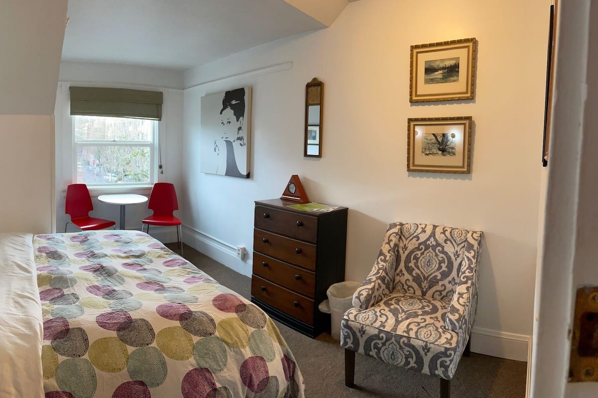 Une chambre à coucher comprenant un lit, une commode, une chaise et une petite table avec deux chaises rouges.