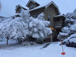 Una casa de dos pisos con un jardín delantero y entrada cubiertos de nieve.