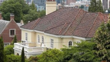 A historic building with a tiled roof, surrounded by well-maintained hedges and a cityscape in the background.