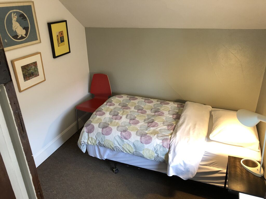 A small, single-bed room with a red chair, a bedside lamp, and framed pictures on the wall.