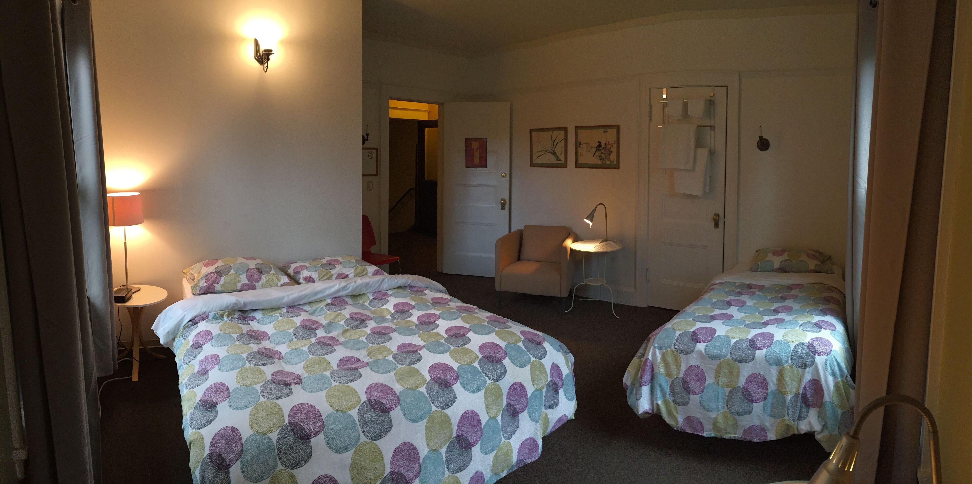 A hotel room with two beds, a chair, a small table, and a lamp.