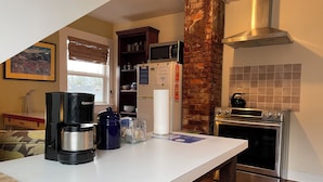 A kitchen with a white countertop, a coffee maker, a kettle, a microwave, and a stove. - Portland International Guesthouse (Portland)