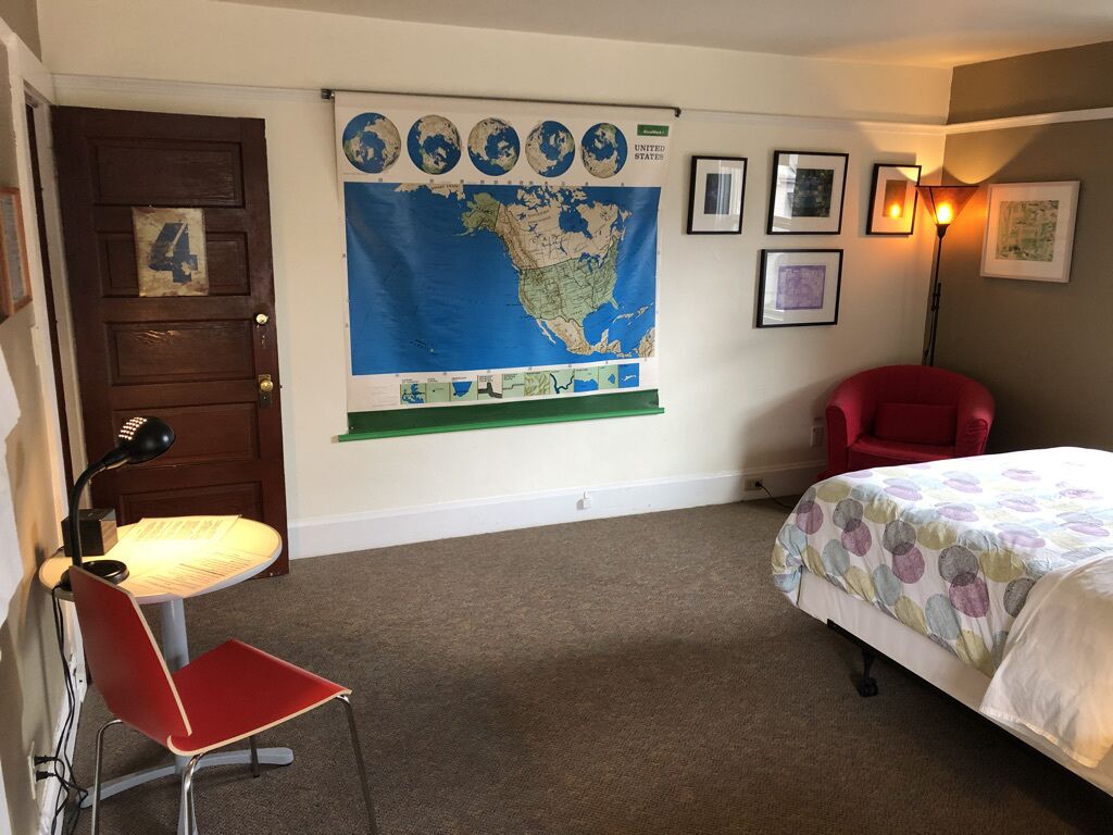 Una habitación con una cama, un escritorio con una silla, un mapa en la pared y una puerta con el número 4.