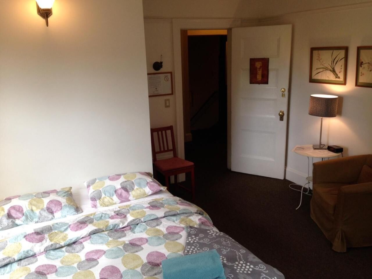 A bedroom with a bed, a chair, a lamp, and a door leading to another room.