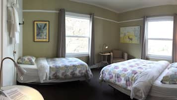 A hotel room with two beds, a small table, a chair, a lamp, and a window with curtains.