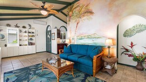 A living room with a blue sofa, a wooden coffee table, a decorative lamp, and a tropical-themed rug.