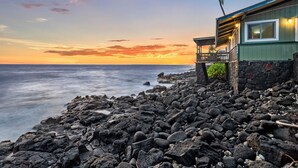 A beachfront property with a stone wall, a wooden structure with a balcony, and a palm tree.
