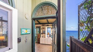 A doorway leading to a room with a view of the ocean, a sign reading "ALOHA", and a small cabinet with various items.