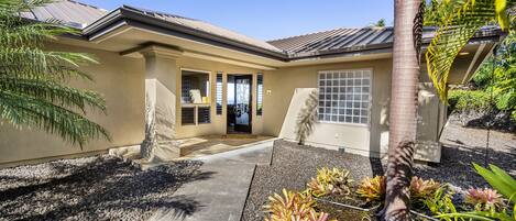 A house with a covered porch, a stone statue, and tropical plants.