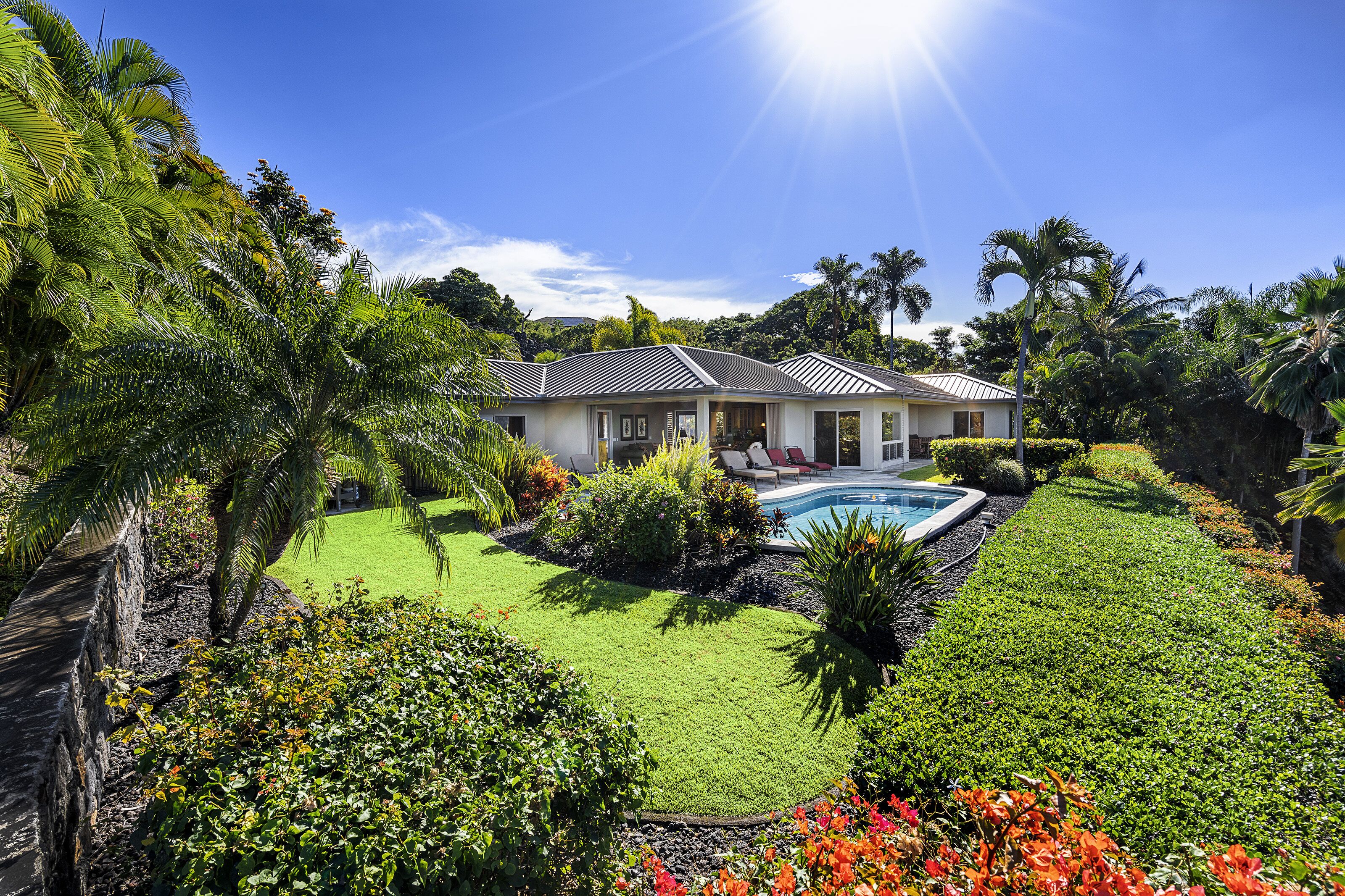A house with a swimming pool surrounded by lush greenery and palm trees.