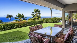 A patio with a table and chairs, overlooking a well-maintained garden and the ocean.