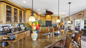 A kitchen with wooden cabinets, a granite countertop, a central island with a sink, and a ceiling fan.