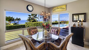 A dining area with wicker chairs, a glass table, and a view of the ocean.