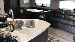 Un intérieur de camping-car compact comprenant un coin cuisine, un espace repas et un coin salon.