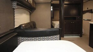 Un intérieur de camping-car compact comprenant un lit, un coin salon et une kitchenette.