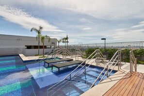 A rooftop swimming pool with a wooden deck, palm trees, and a city view. - 123 Expo Anhembi (São Paulo)
