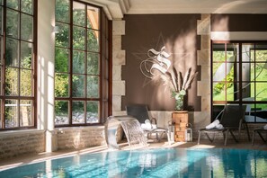 A pool area with a waterfall feature, a lounge chair, and a decorative wall with a geometric design. - Hotel ZUM STERNENHOF (Koessen)