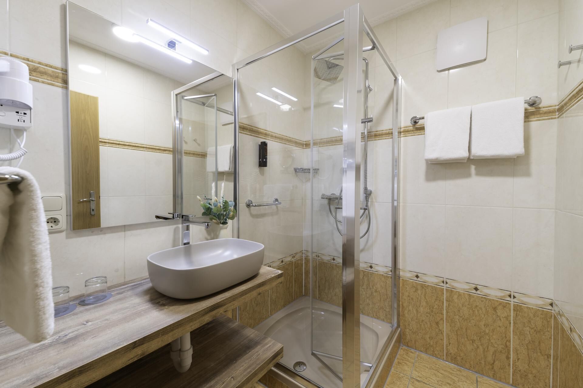 Uma casa de banho moderna com chuveiro envolto em vidro, pia branca e espelho.