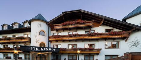 A multi-story hotel with balconies adorned with flowers, a sign reading "Zum Sternenhof Wellness Hotel," and a star-shaped emblem on the facade.