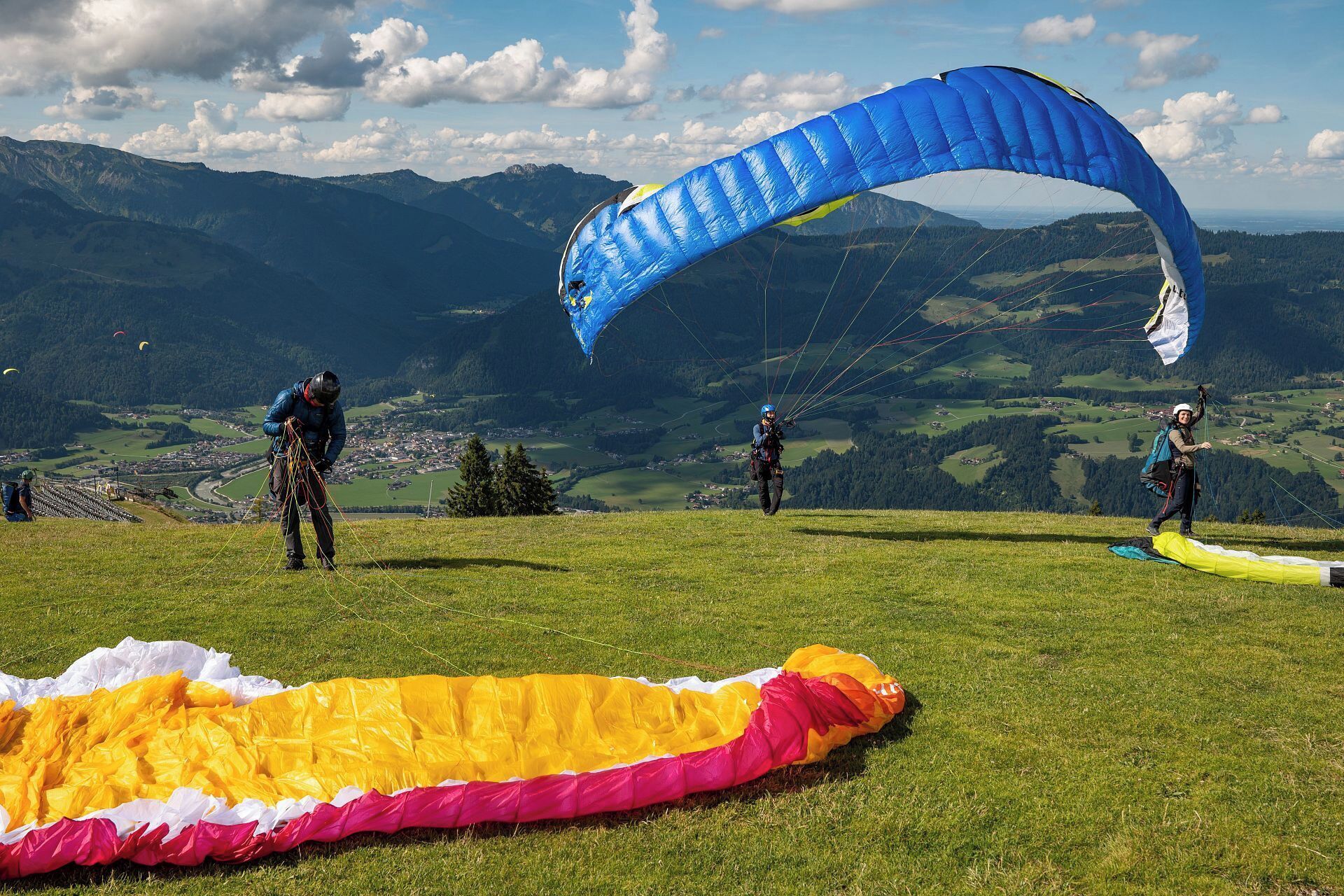A grassy field with a large blue parachute and a yellow and pink one on the ground.