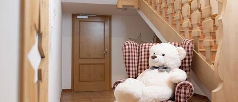 Un osito de peluche blanco y mullido sentado en un sillón a cuadros en un pasillo con una escalera de madera.