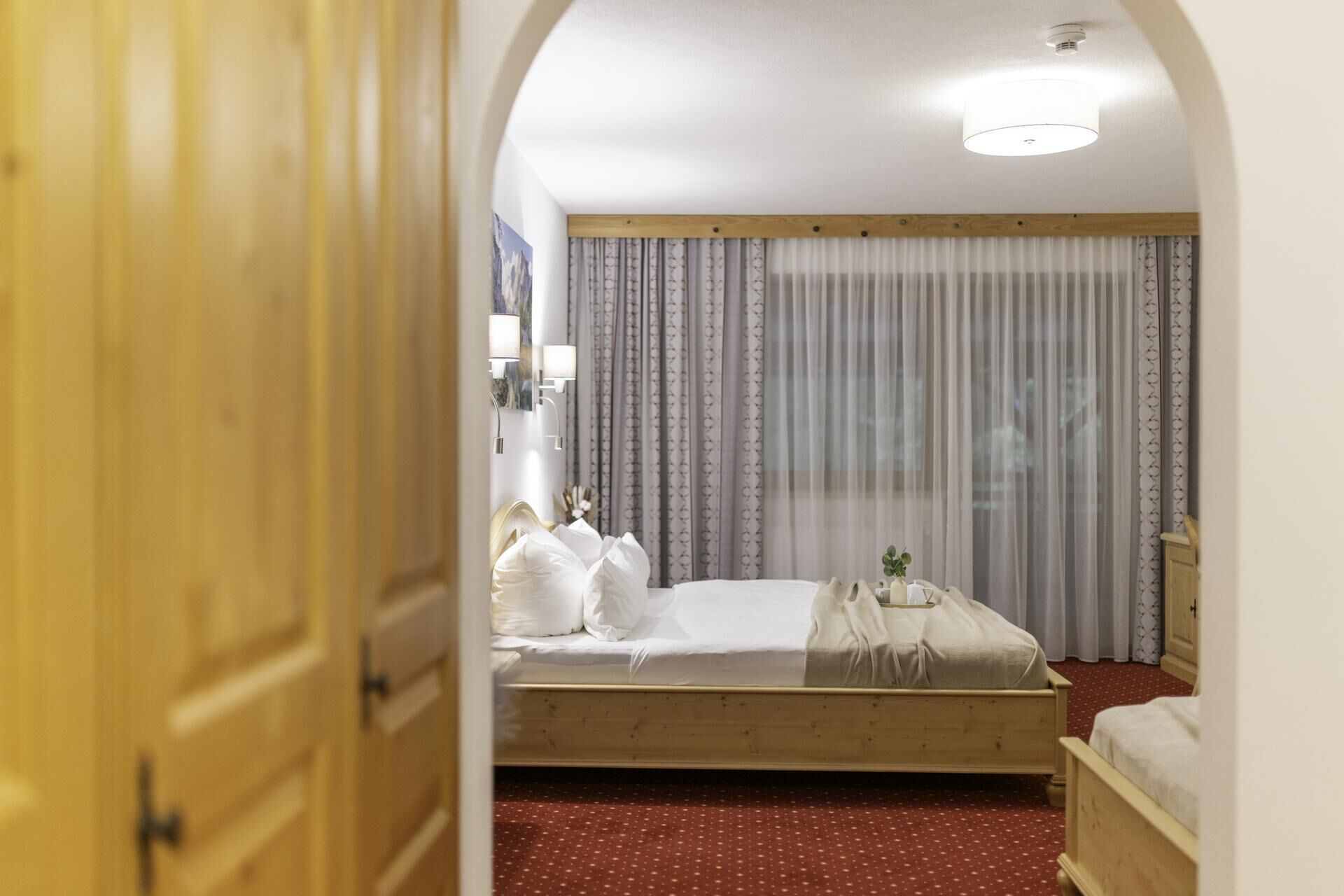 A hotel room with a wooden bed, a small bedside table, a mirror, and a window with curtains.