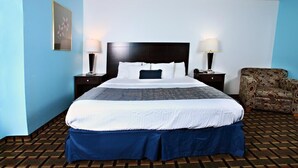 Une chambre d’hôtel avec un grand lit, deux tables de chevet avec des lampes, un fauteuil à motifs et une moquette à motifs.