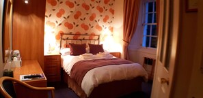A small, cozy bedroom with a bed, bedside table, and a chair. The room has a floral wallpaper and a window with curtains. - Creag Dhubh Country House (Inveraray)