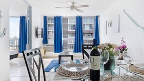 A dining area with a table set for two, a bottle of wine, and a vase with flowers.