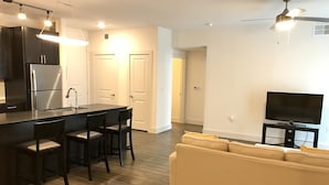 Una cocina moderna con una isla central, un comedor con sillas, un sofá y un televisor en la sala de estar.