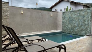 Une piscine avec des chaises longues, un mur de pierre et un bâtiment en arrière-plan.
