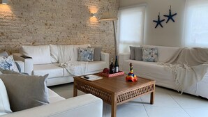 Un salon avec deux canapés blancs, une table basse en bois et un mur décoré d’un motif en briques.