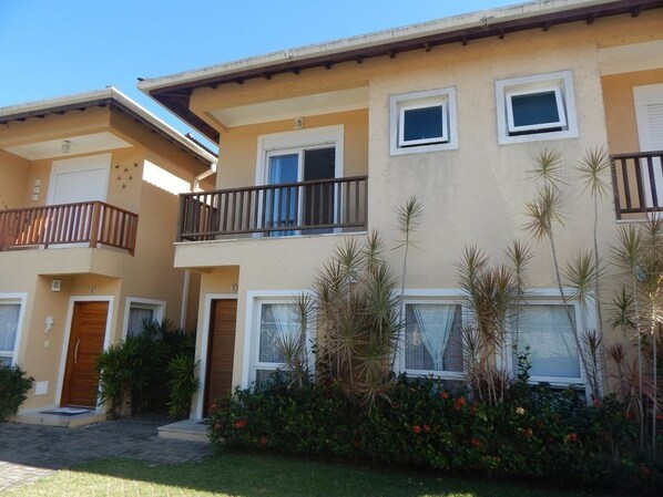 A multi-story residential building with balconies, windows, and a well-maintained garden. - Spacious and comfortable house in a gated community, private pool, beach service. (São Sebastião)