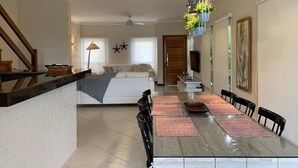 Une cuisine moderne avec un plan de travail noir, un mur de briques blanches derrière l’évier et un coin repas comprenant une table en verre et des chaises noires.