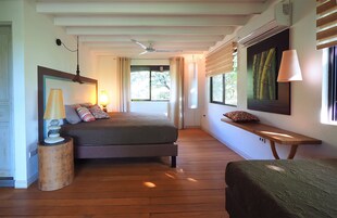 A bedroom with a bed, bedside table, lamp, and a window with blinds.