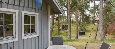 A wooden deck with a stone table and two chairs, a flag, and a view of a forested area.