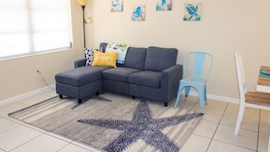 A living room with a grey sectional sofa, a star-patterned rug, a blue chair, and wall art. - BEACH TIME! WALK/BIKE TO THE BEACH-Min to shops, dining, movies-Fenced backyard (Naples)