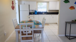 A kitchen with white cabinets, a wooden dining table with chairs, a refrigerator, and a window with blinds. - BEACH TIME! WALK/BIKE TO THE BEACH-Min to shops, dining, movies-Fenced backyard (Naples)