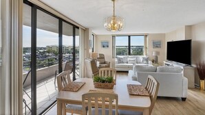 A spacious living area with a balcony, large windows, and a modern chandelier. - Anchorage Resort 7th Floor 2-Bedroom Condo w Private Balcony Beach Access (Siesta Key)
