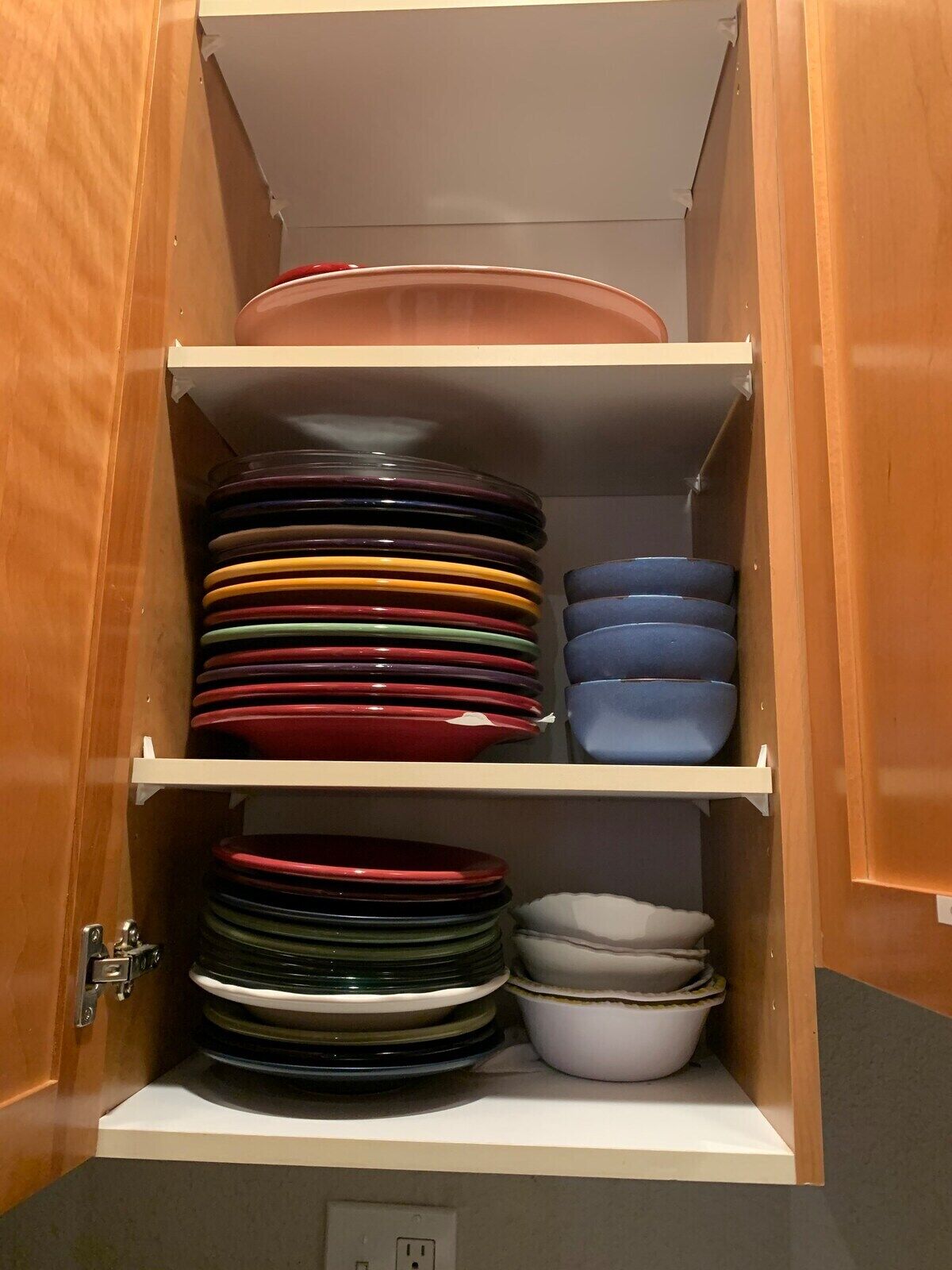 A cabinet with multiple shelves containing various colored plates and bowls.
