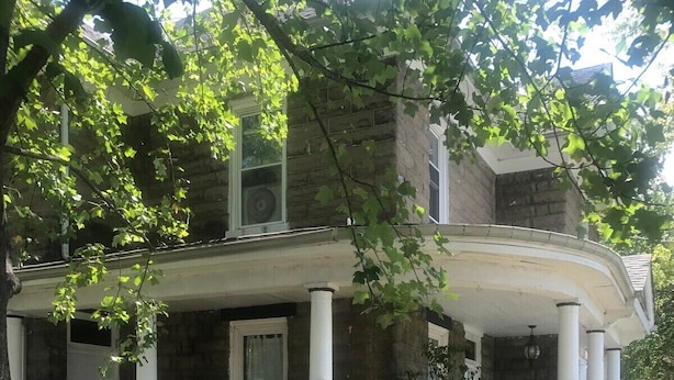 A two-story house with a covered porch, stone exterior, and a large tree in the foreground. - Pet and kid friendly duplex with 2 bedrooms (Pacific)