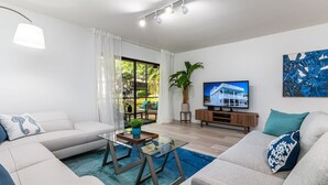Een moderne woonkamer met een bank, een salontafel, een televisie en een groot raam met gordijnen.