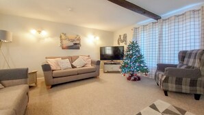 Ein Wohnzimmer mit einer Couch, einem Fernseher, einem Weihnachtsbaum und einem gemusterten Teppich.